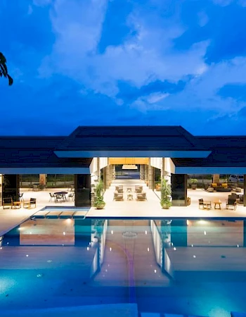 A modern building with open spaces and a large swimming pool, illuminated at night.