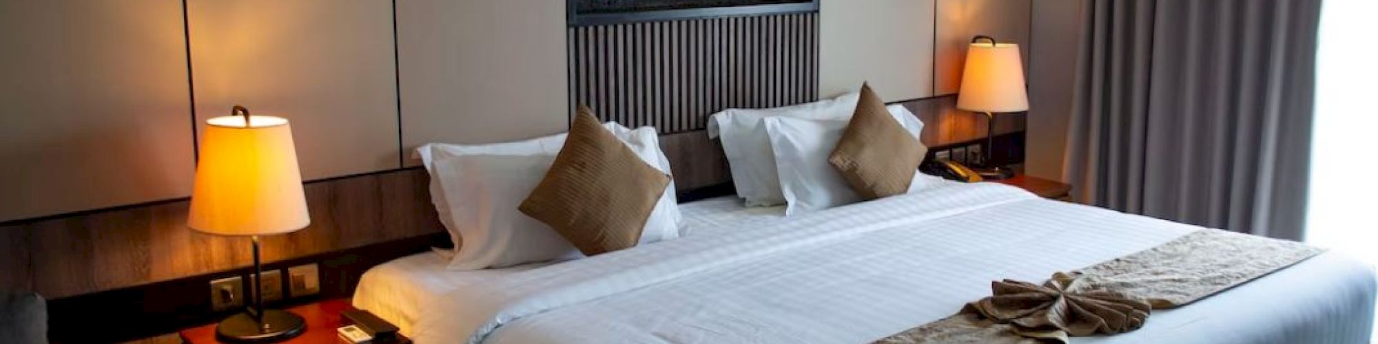 A cozy hotel room featuring a large bed with pillows, bedside lamps, and a window with curtains.