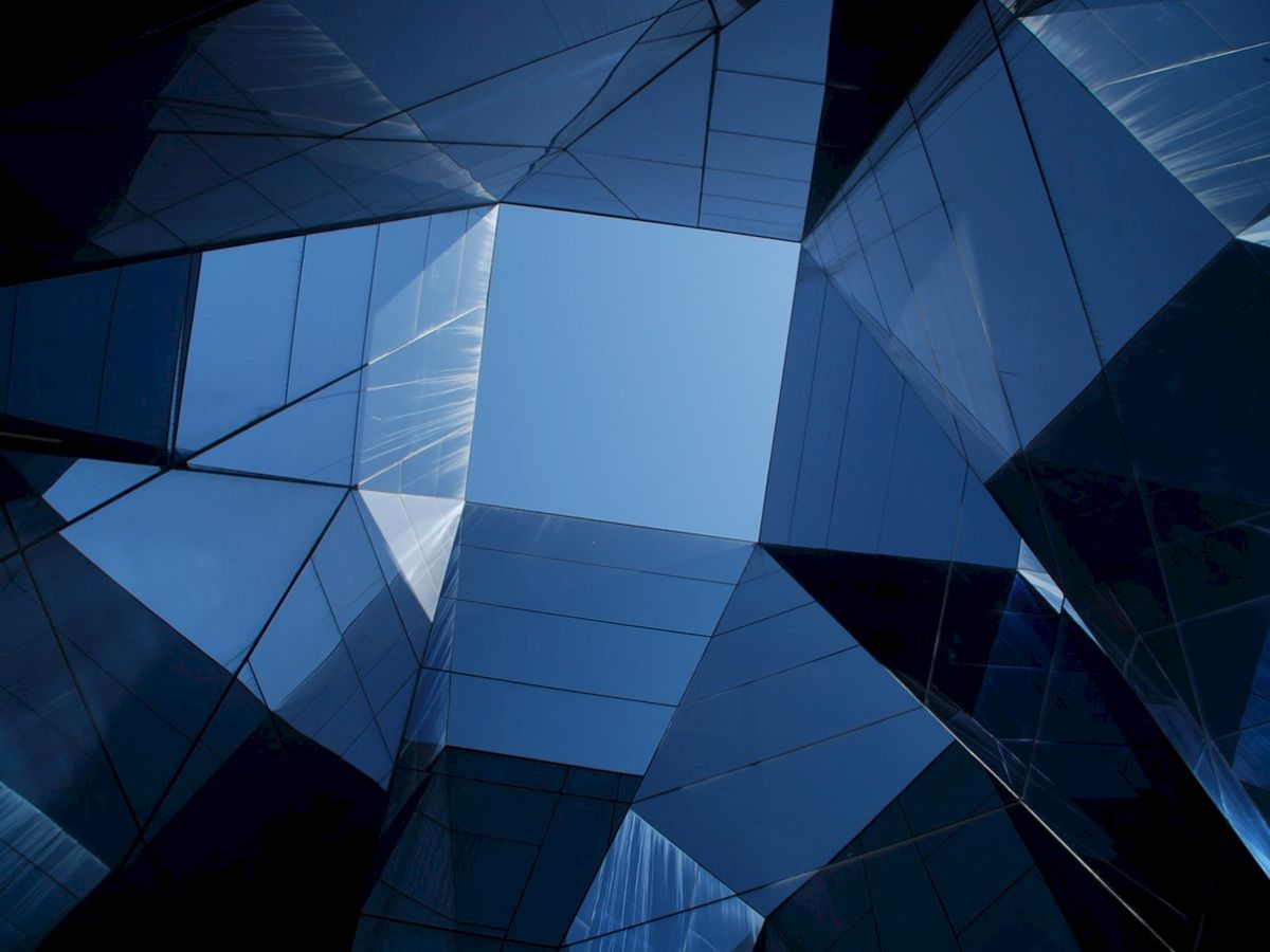 A modern architectural structure with glass panels reflecting light, creating a geometric pattern against a blue sky.
