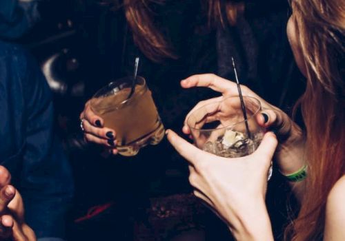 People are having a good time, holding drinks and smiling. It looks like a social gathering or party setting, with an energetic atmosphere.
