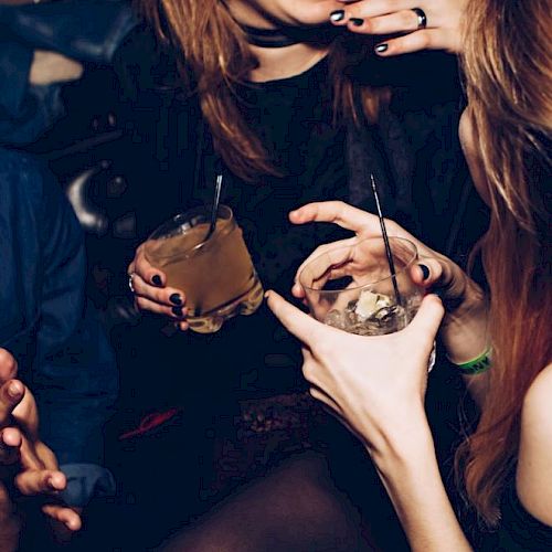 People are having a good time, holding drinks and smiling. It looks like a social gathering or party setting, with an energetic atmosphere.