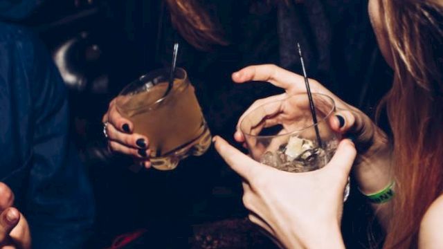 People are having a good time, holding drinks and smiling. It looks like a social gathering or party setting, with an energetic atmosphere.