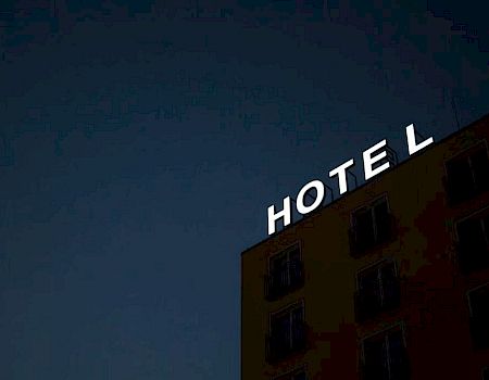 A building with a bright white "HOTEL" sign against a dark sky background, partial view of the facade.