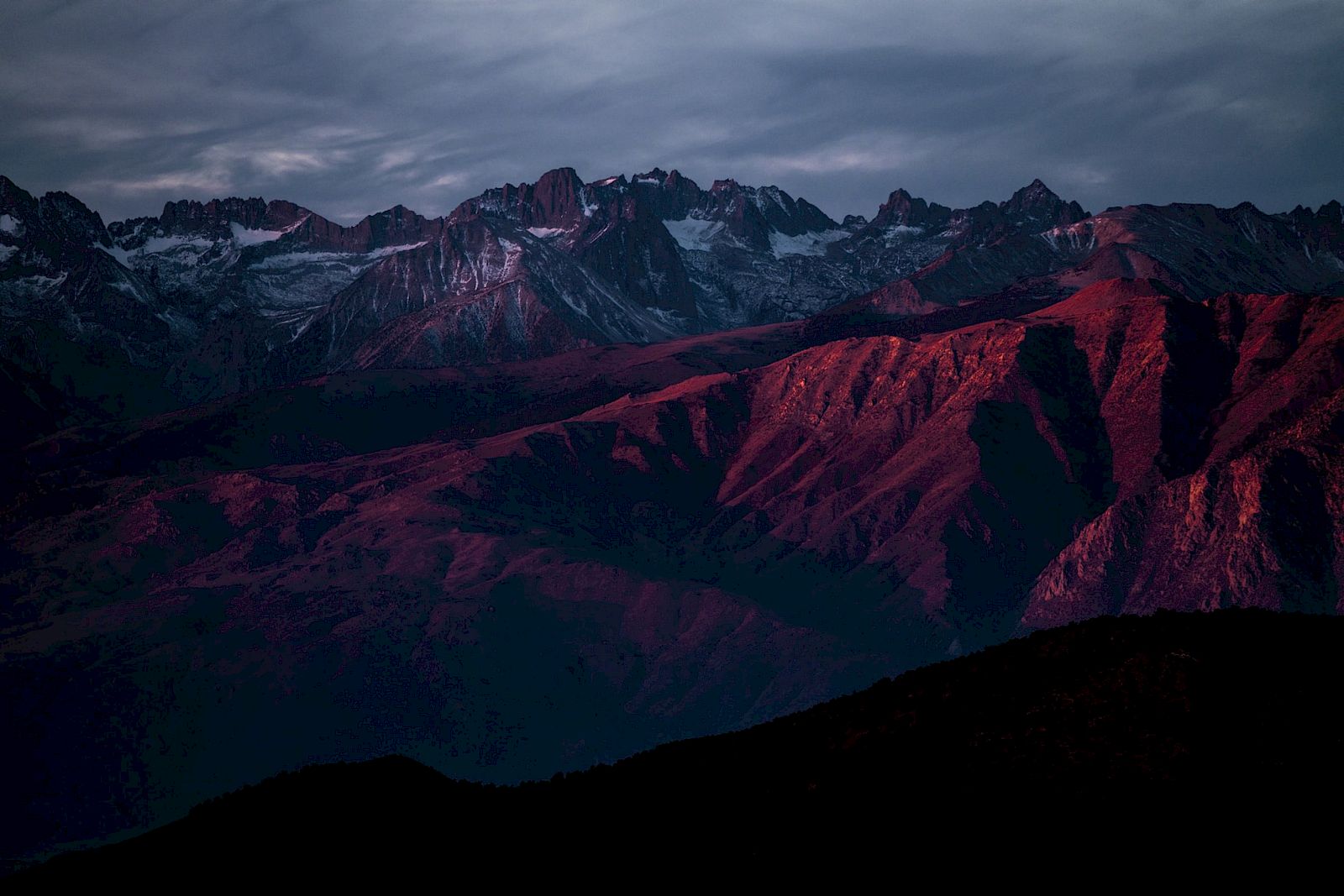 A mountain range bathed in red sunset light under a moody, cloudy sky.