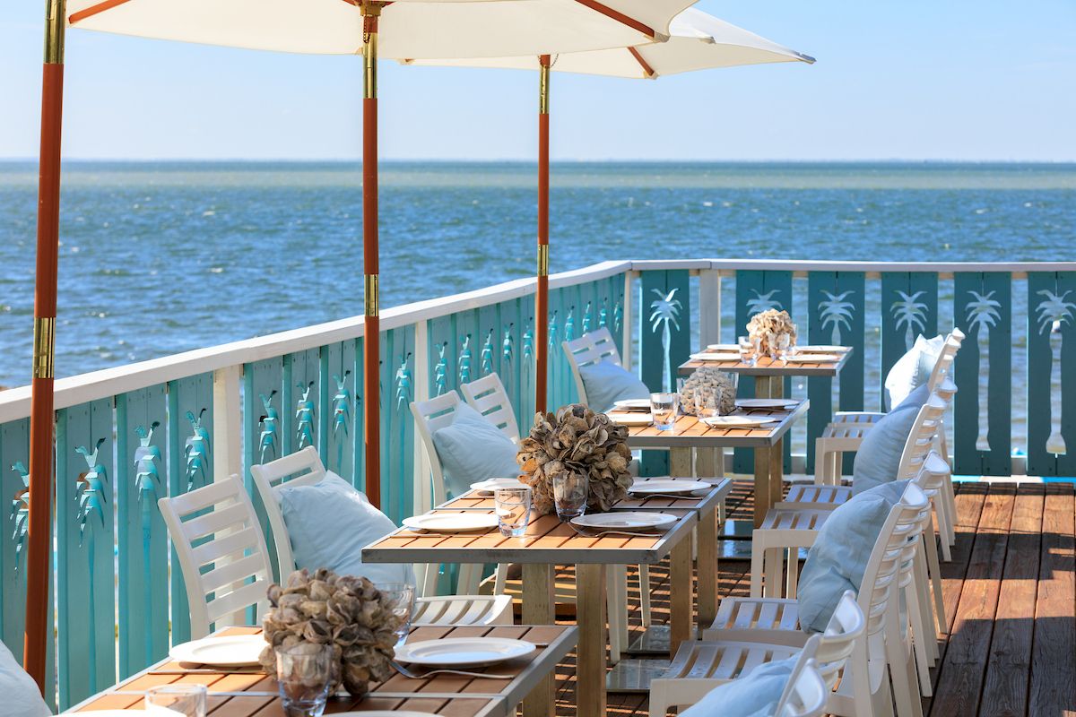 A seaside restaurant patio with tables set under umbrellas, overlooking the ocean, featuring decorative elements and a relaxed atmosphere.