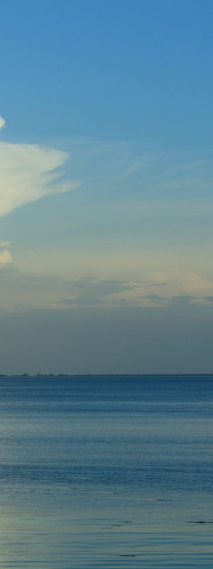 A calm sea with a clear blue sky, a small distant cloud, and gentle horizon&mdash;serene coastal scene.