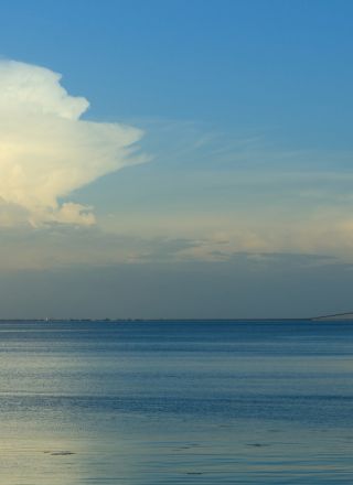 A calm sea with a clear blue sky, a small distant cloud, and gentle horizon&mdash;serene coastal scene.