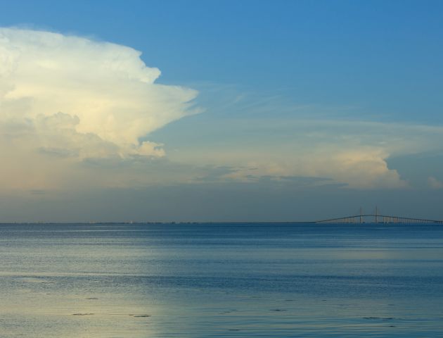 A calm sea with a clear blue sky, a small distant cloud, and gentle horizon&mdash;serene coastal scene.