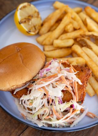 A burger topped with coleslaw and sauce, served with fries and a lemon slice on a plate.