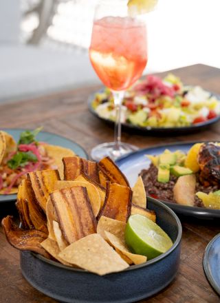 A colorful meal spread with grilled fries in a bowl, taco-style sides, and a pink sparkling drink topped with a lime.