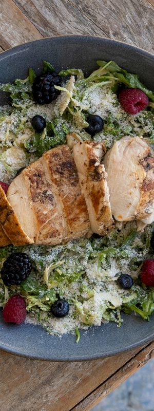A plate of sliced chicken on a salad with berries and grated cheese, set on a wooden table.