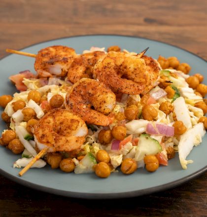 A bowl of mixed salad topped with grilled chicken, crispy chickpeas, and chopped veggies on a wooden table.