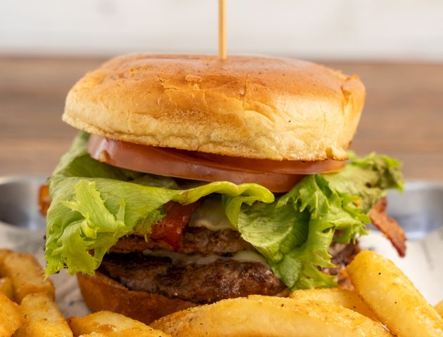 A cheeseburger with lettuce and tomato sits atop crispy fries, with a cheese layer pouring over the top.