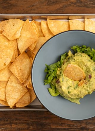 A tray of tortilla chips with a bowl of guacamole topped with lettuce on a wooden table.