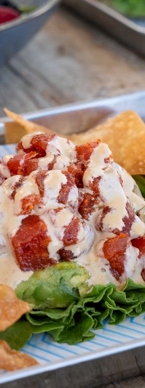 A dish with crispy chips, lettuce, diced tomatoes, and a creamy sauce drizzle is presented on a metal tray.