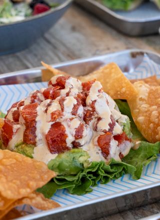 A dish with crispy chips, lettuce, diced tomatoes, and a creamy sauce drizzle is presented on a metal tray.