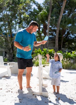 A man and a child are playing on a sandy beach, blowing bubbles or playing with a toy.
