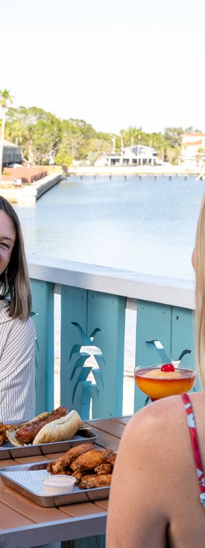 Two people are enjoying drinks and food on a waterfront patio.