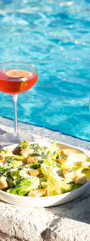 Poolside setting with shrimp, salad, berries with cream, and three drinks: blue cocktail, orange cocktail, and wine.