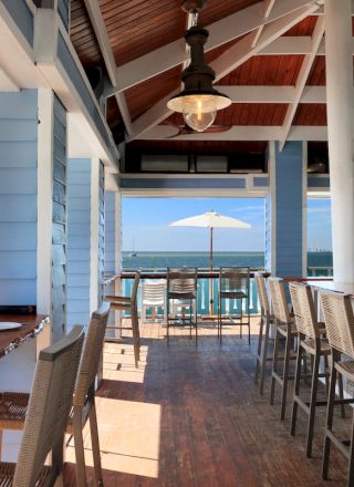 A bright indoor dining area with wooden tables and chairs, large windows, and a view of the outdoors, daylight streaming in, inviting ambiance.