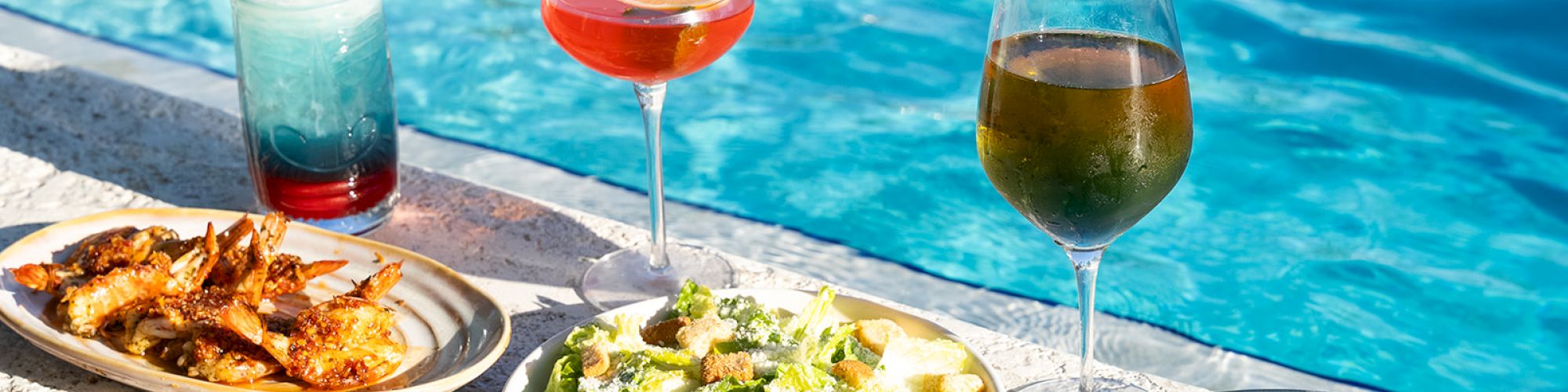 Poolside meal with shrimp, salad, and drinks. Refreshing cocktails and wine accompany the vibrant dishes.