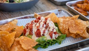 A dish with diced tuna in sauce, served on lettuce with fried wonton chips around it, presented on a metal tray.