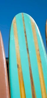 Colorful surfboards lined up against a blue sky, each with bold stripes and glossy finishes, ready for a sunny day at the beach.