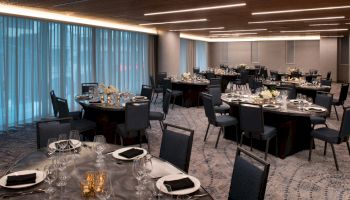 The image shows a modern banquet hall with round tables set for an event, featuring dim lighting and elegant black chairs.