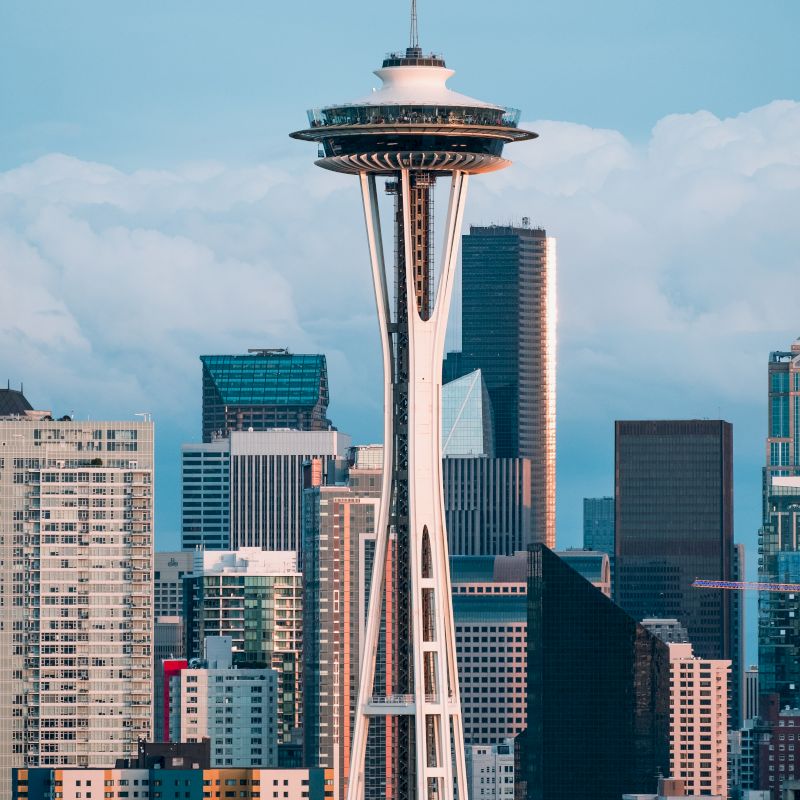 The image shows the Space Needle with surrounding city skyscrapers against a cloudy sky in Seattle, Washington.