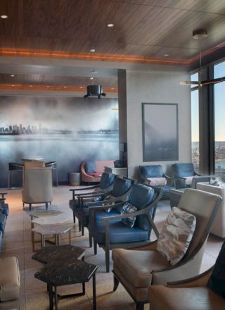 A modern lounge with stylish seating, large windows offering a scenic water view, and a wall mural depicting a city skyline.