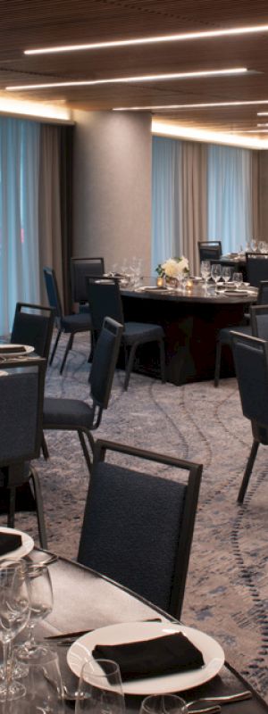 The image shows an elegant dining room setup with round tables, chairs, and table settings, including napkins and wine glasses.