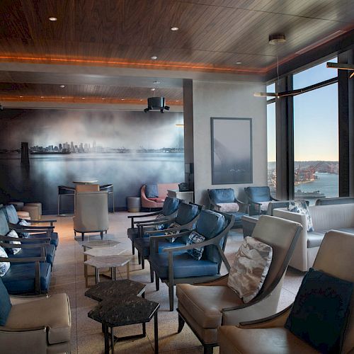 A stylish lounge with leather chairs, large windows, a scenic view, and a wall mural depicting a city skyline under soft lighting.