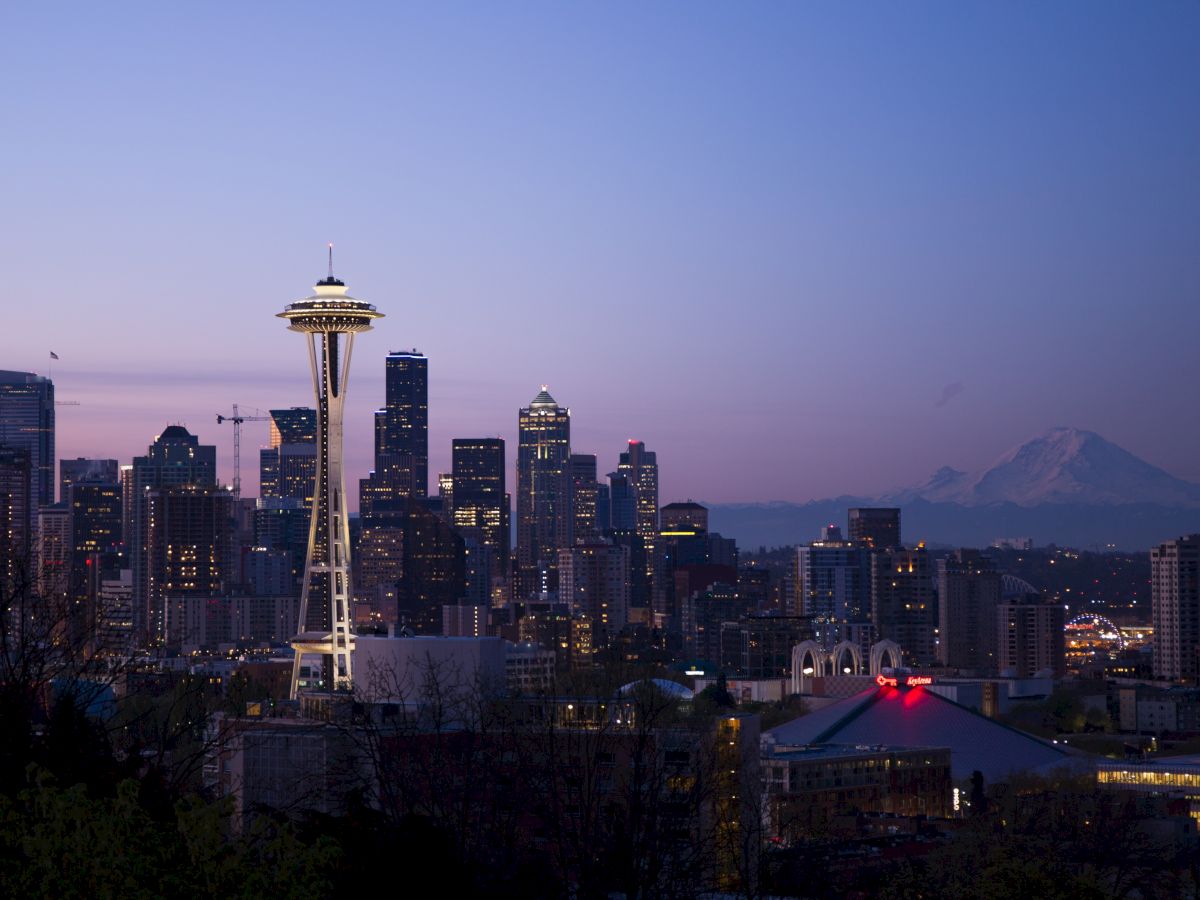 Seattle skyline at dusk with the Space Needle and Mount Rainier in the background, under a clear sky.