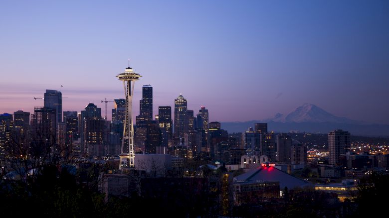 Seattle skyline at dusk with the Space Needle and Mount Rainier in the background, under a clear sky.